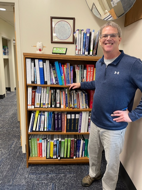 VU professor Kirk Abendroth stands next to a book shelf